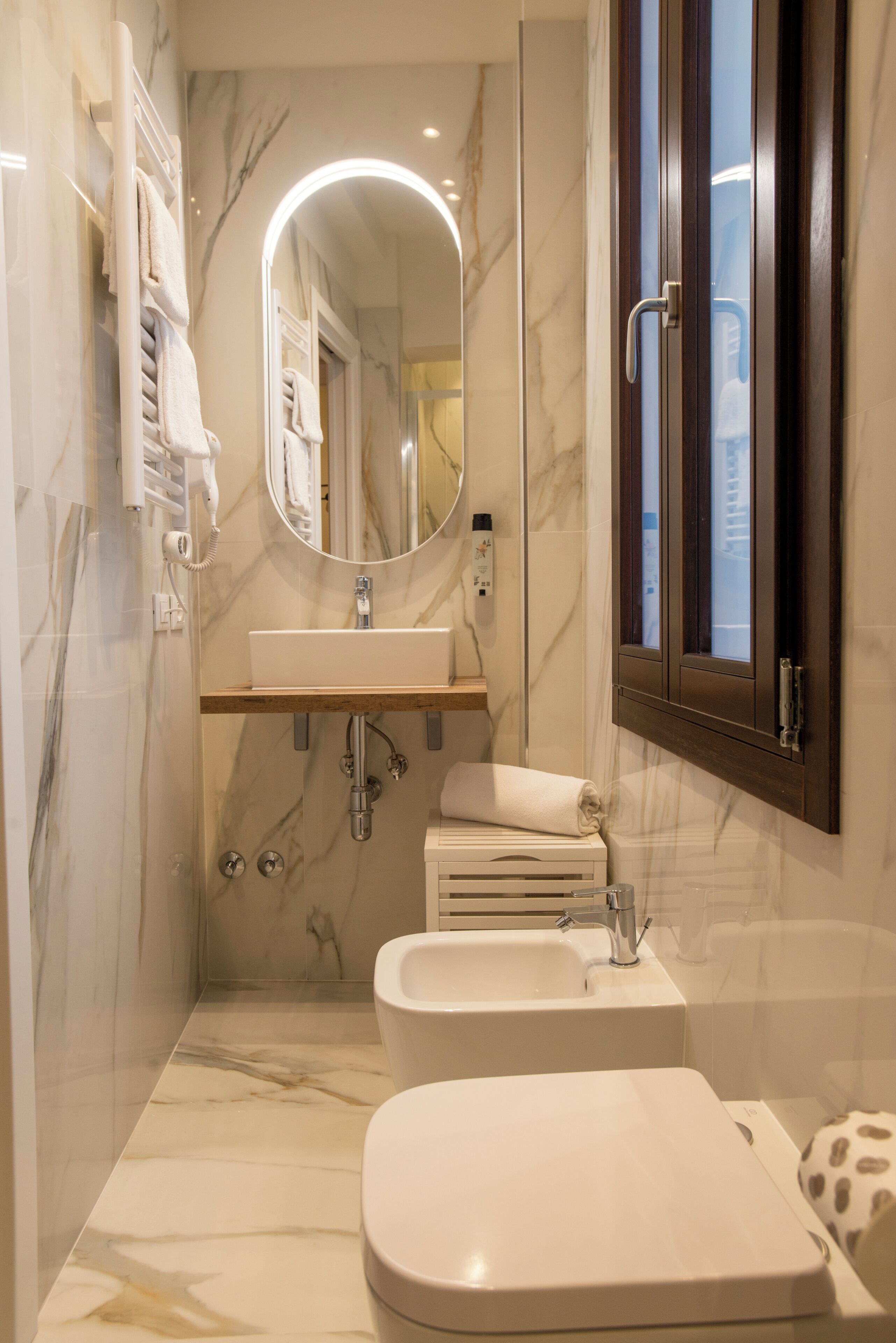 Une salle de bain avec un mur en marbre, un lavabo, des toilettes, un miroir et une fenêtre.