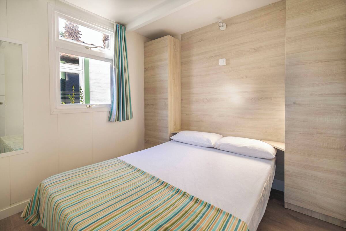 Een slaapkamer met een bed, een raam met gordijnen en een houten hoofdbord.