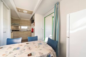 Une cuisine compacte avec des meubles en bois, un four à micro-ondes et une cuisinière à gaz. On y trouve un coin repas avec une table et des chaises, et un réfrigérateur sur la droite.