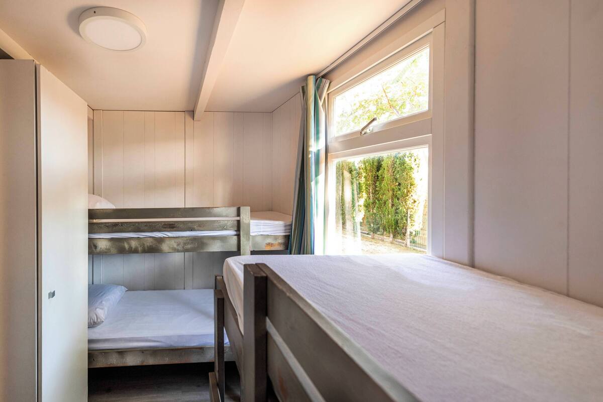 Een kleine kamer met stapelbedden en een raam met uitzicht op groen.