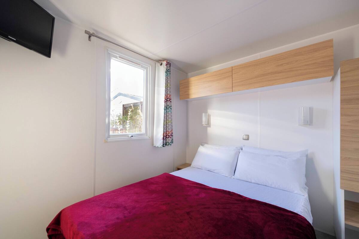 Een slaapkamer met een bed, een raam en ingebouwde houten kasten.
