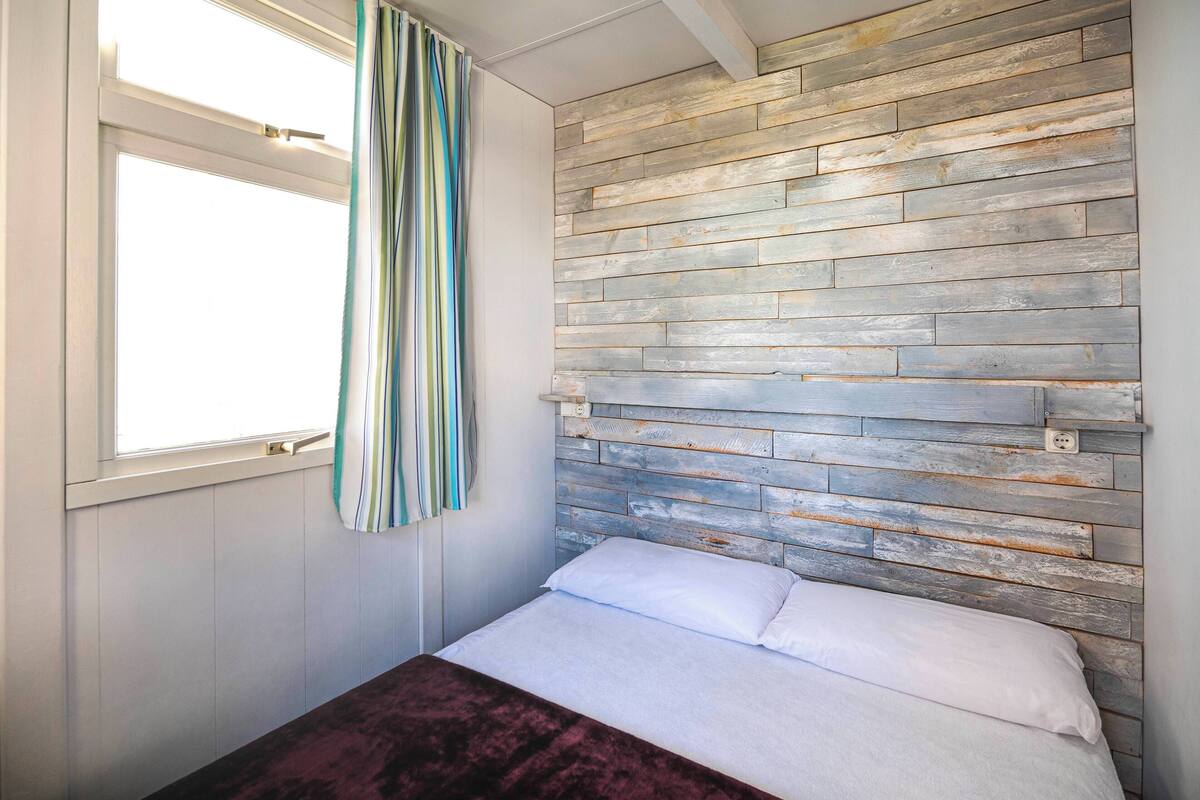 Een slaapkamer met een bed, een raam met gordijnen en een houten hoofdbord.