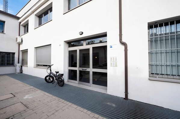 Un edificio blanco con un gran portón de garaje, una bicicleta estacionada afuera y una reja metálica en el suelo.