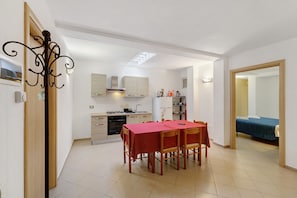 Une cuisine compacte avec un coin repas, un petit espace de vie et une chambre à coucher visible à travers une porte ouverte.