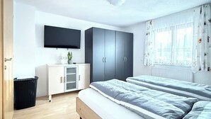 Moderni makuuhuone, jossa on sänky, televisio, vaatekaappi ja työpöytä.