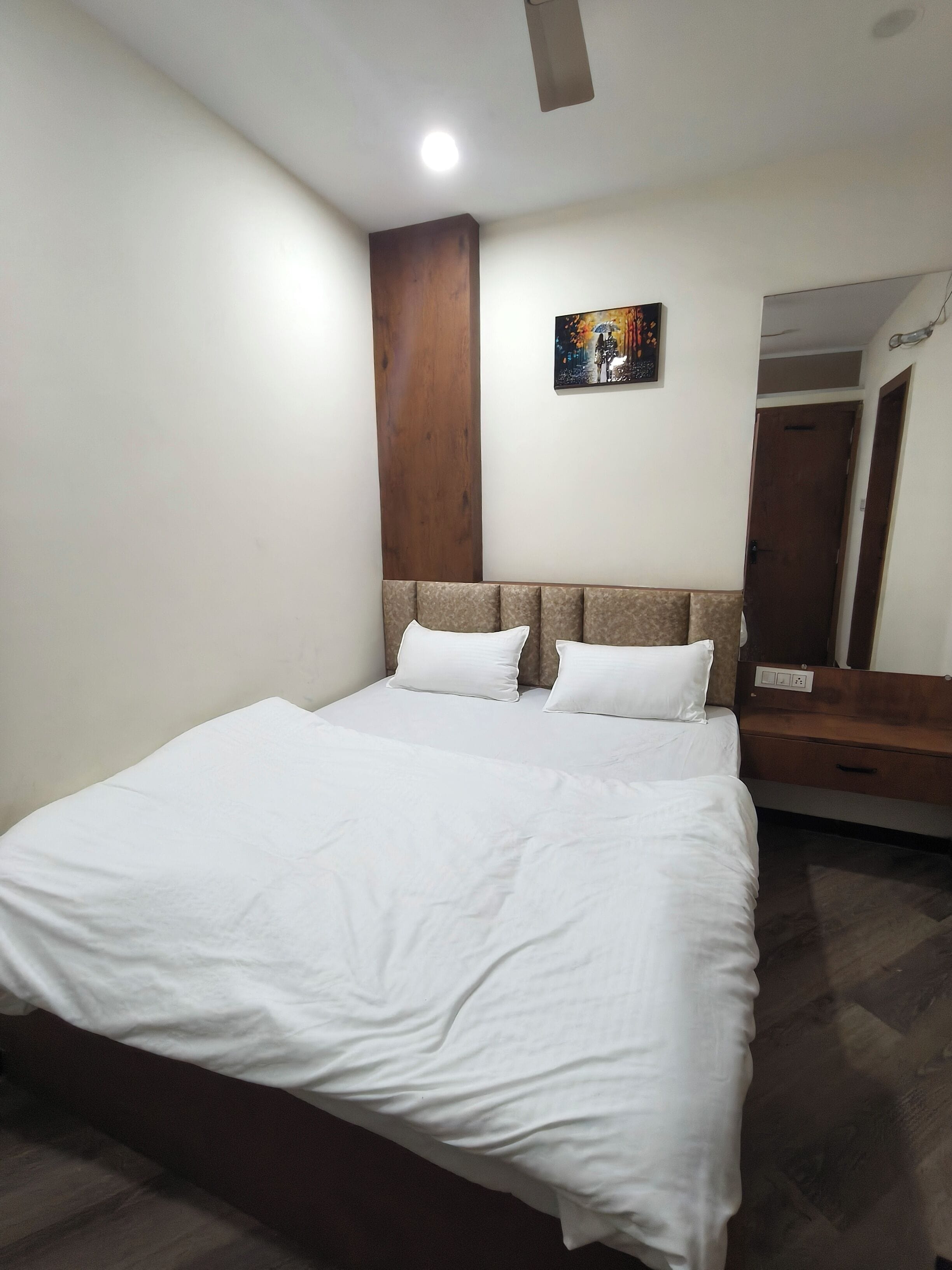 Una cama bien hecha con sábanas blancas en una habitación con cabecera de madera y un cuadro en la pared.