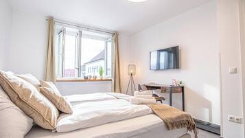 A bedroom with a bed, a desk, a TV, and a window with curtains.