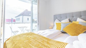 Ein Schlafzimmer mit Bett, einem Balkon mit Blick auf Gebäude und einem Fenster.