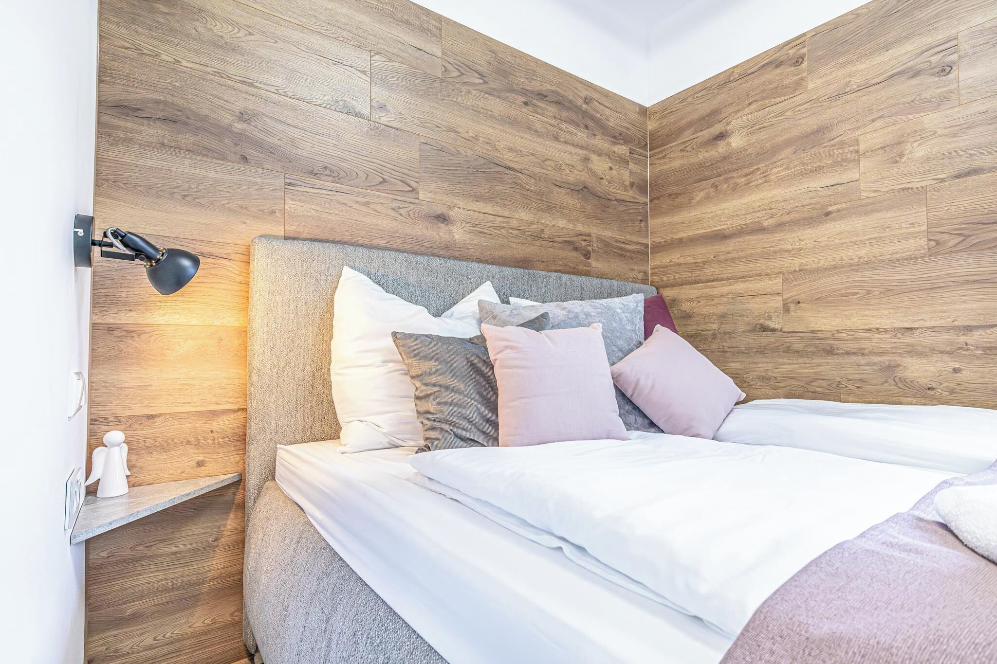 Een slaapkamer met een houten hoofdbord, een bedlampje en een opgemaakt bed met meerdere kussens.
