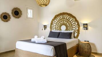 Een slaapkamer met een groot bed, een decoratief hoofdbord, twee wandlampen en een rond geweven bijzettafeltje.
