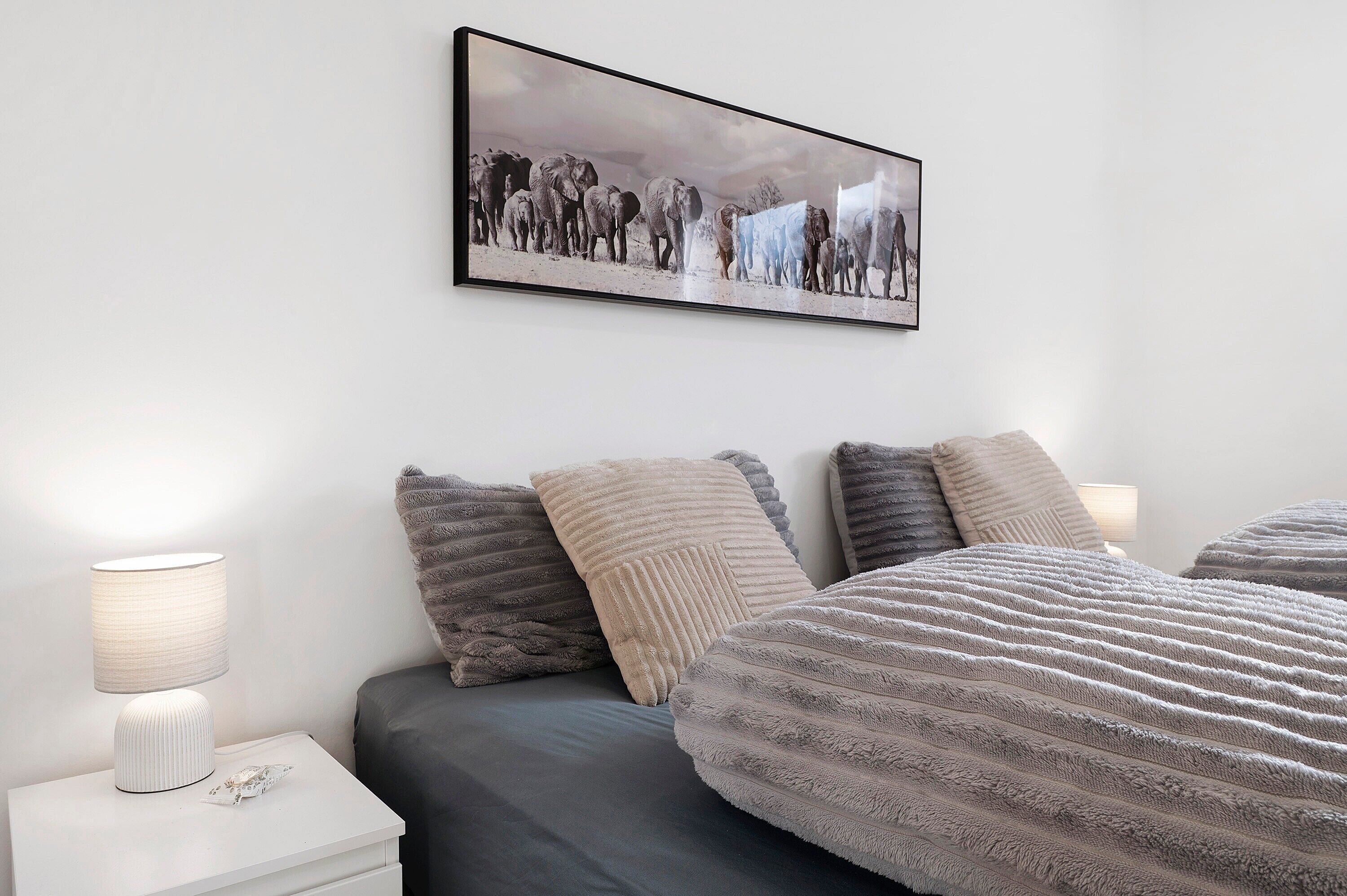 Una camera da letto con un letto, cuscini, un comodino con una lampada e un quadro appeso al muro.
