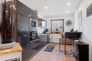 A modern kitchen with a microwave, oven, and a dining area with a bar stool. - Apartment “Landhaus Sonnenterrasse” with Private Terrace, Garden, and Wi-Fi (Grasberg)