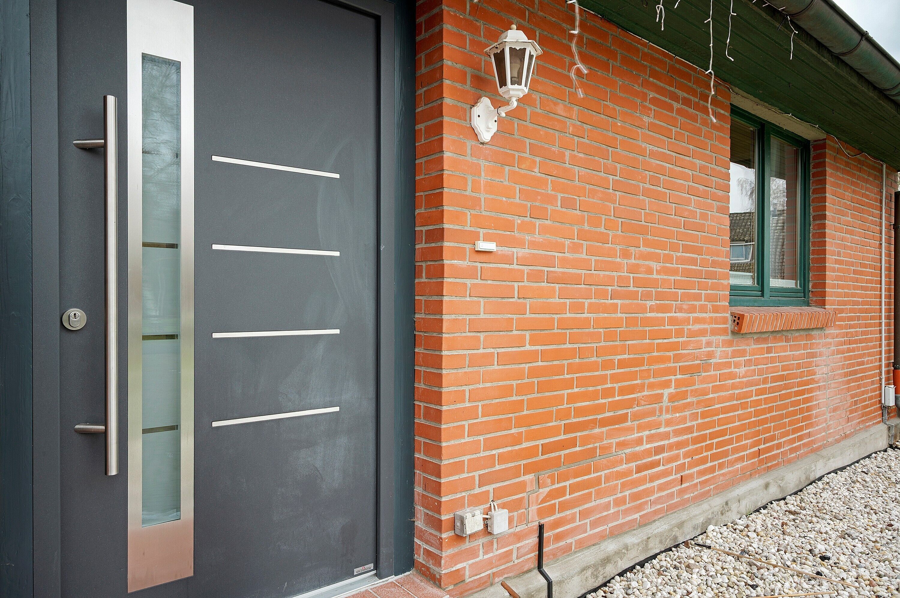 Een modern gebouw met een donkere deur, een gevel van baksteen en een raam met een groene omlijsting.