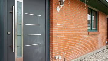 Een modern gebouw met een donkere deur, een gevel van baksteen en een raam met een groene omlijsting.