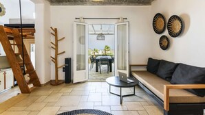 Ein modernes Wohnzimmer mit einer Holztreppe, einer Couch, einem Essbereich mit Tisch und Stühlen sowie einem Blick durch eine Glastür auf eine Terrasse.
