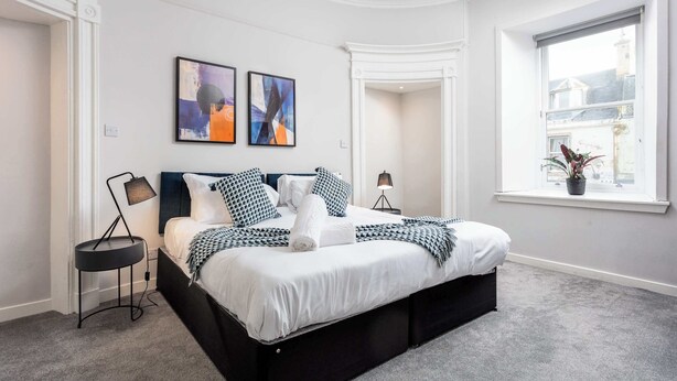 A modern bedroom with a large bed, two bedside tables, and a window with a view of buildings. - The Annick Suite No1 - Donnini Apartments (Irvine)