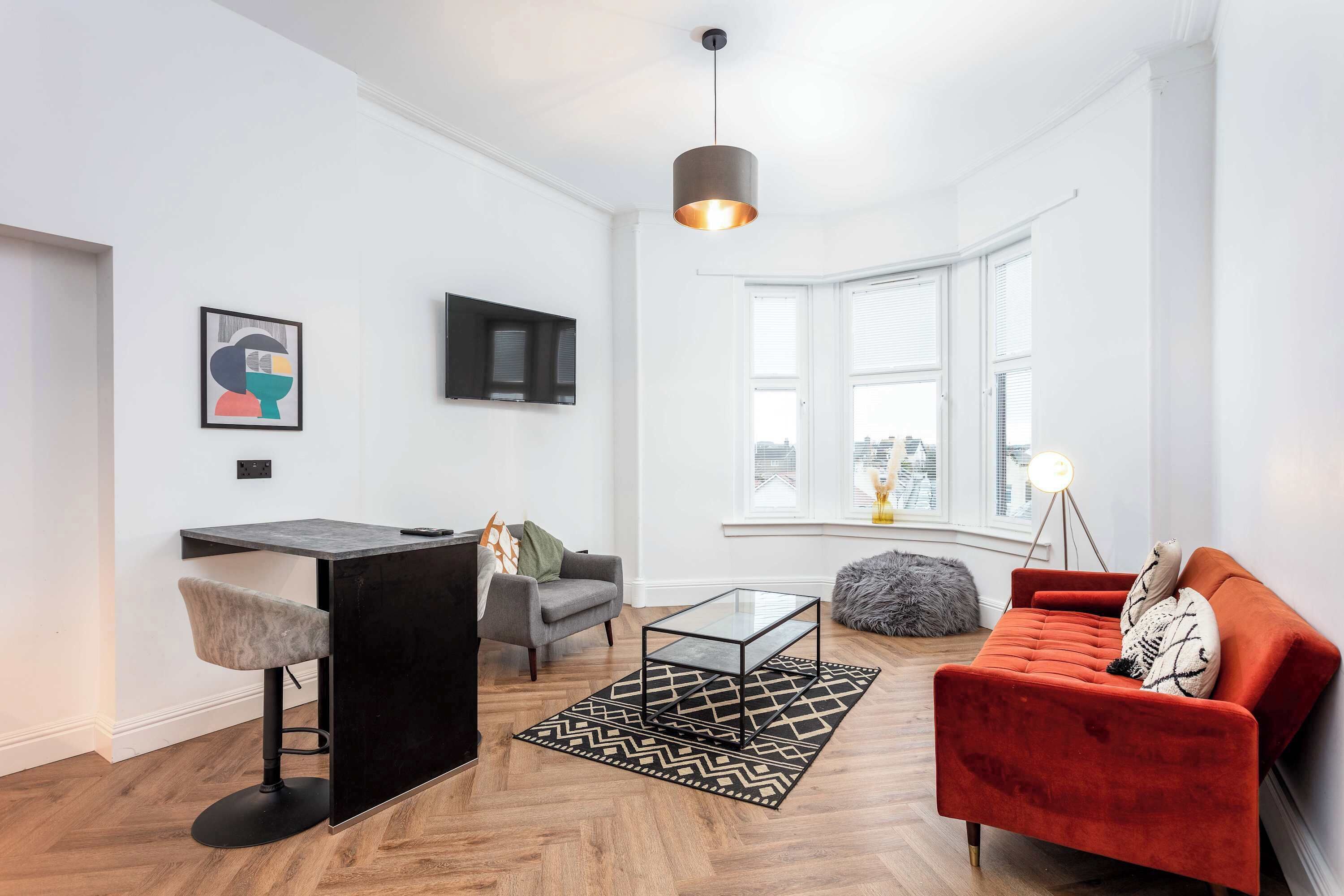 Uma sala de estar moderna com um banquinho preto, um sofá vermelho, uma mesa de centro de vidro e um tapete com padrão preto e branco.