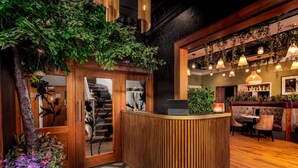 Zona de recepción con mostrador de madera, una escalera y un área de descanso con lámparas colgantes.