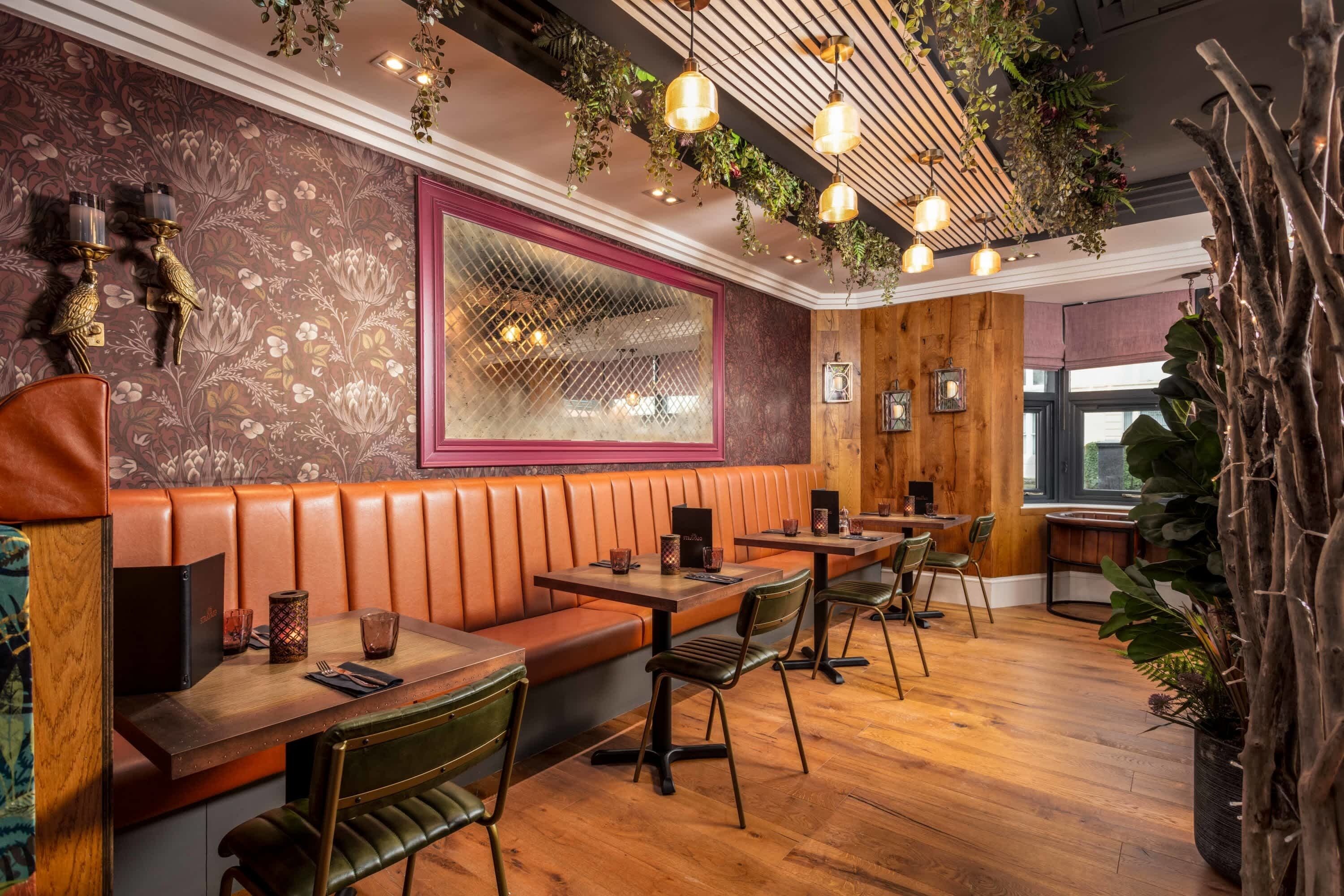 Een restaurant met houten banken, groene stoelen en een behang met patroon.
