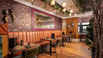 Een restaurant met houten banken, groene stoelen en een behang met patroon.