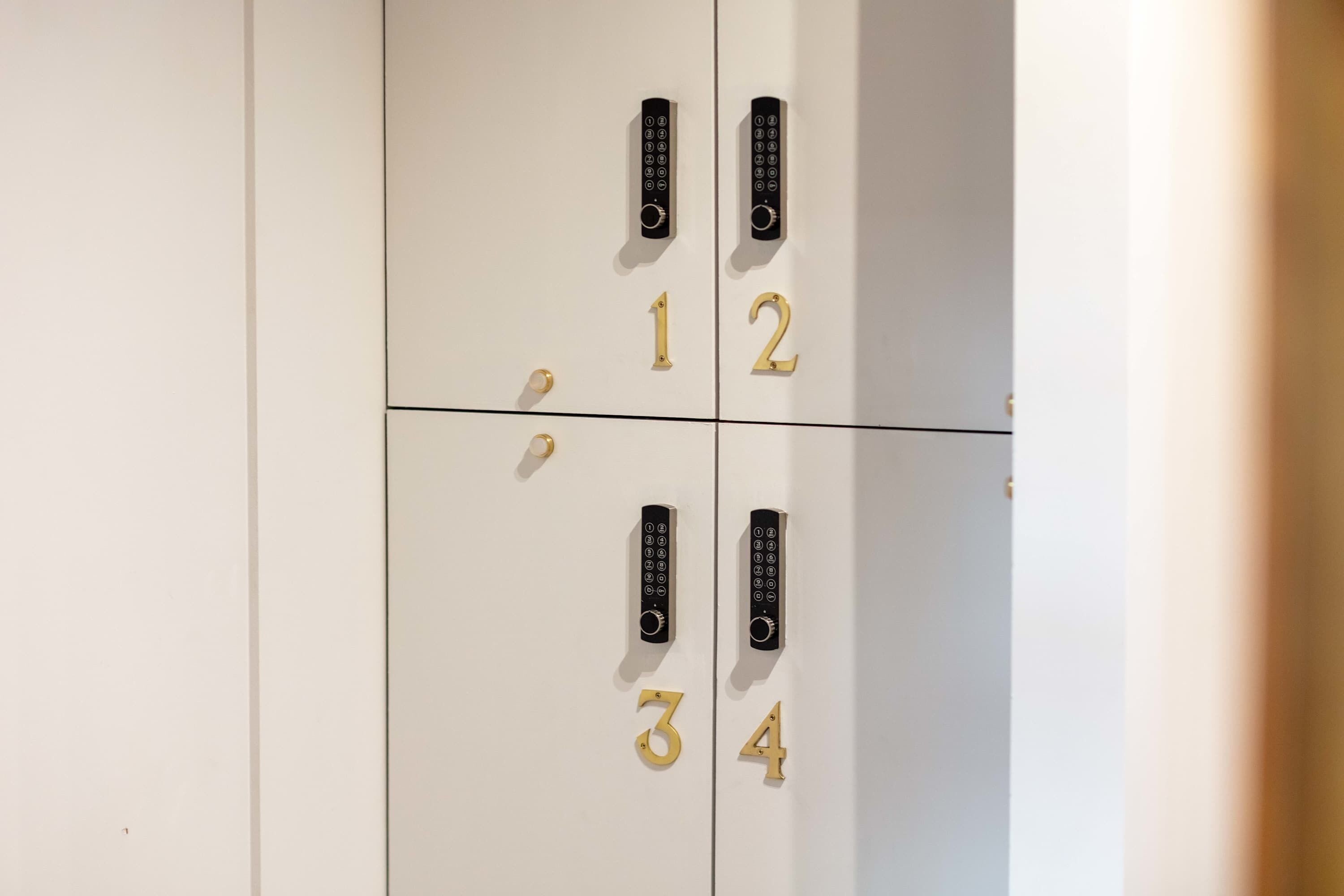 A set of four white lockers with black keypads and gold numbers 1 to 4.