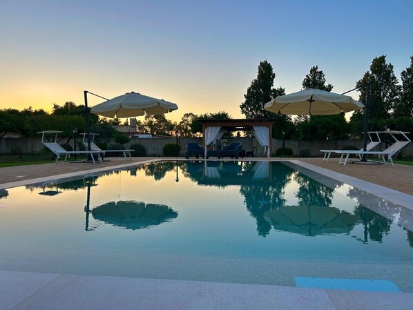 A swimming pool with lounge chairs and umbrellas, surrounded by trees and a pergola.