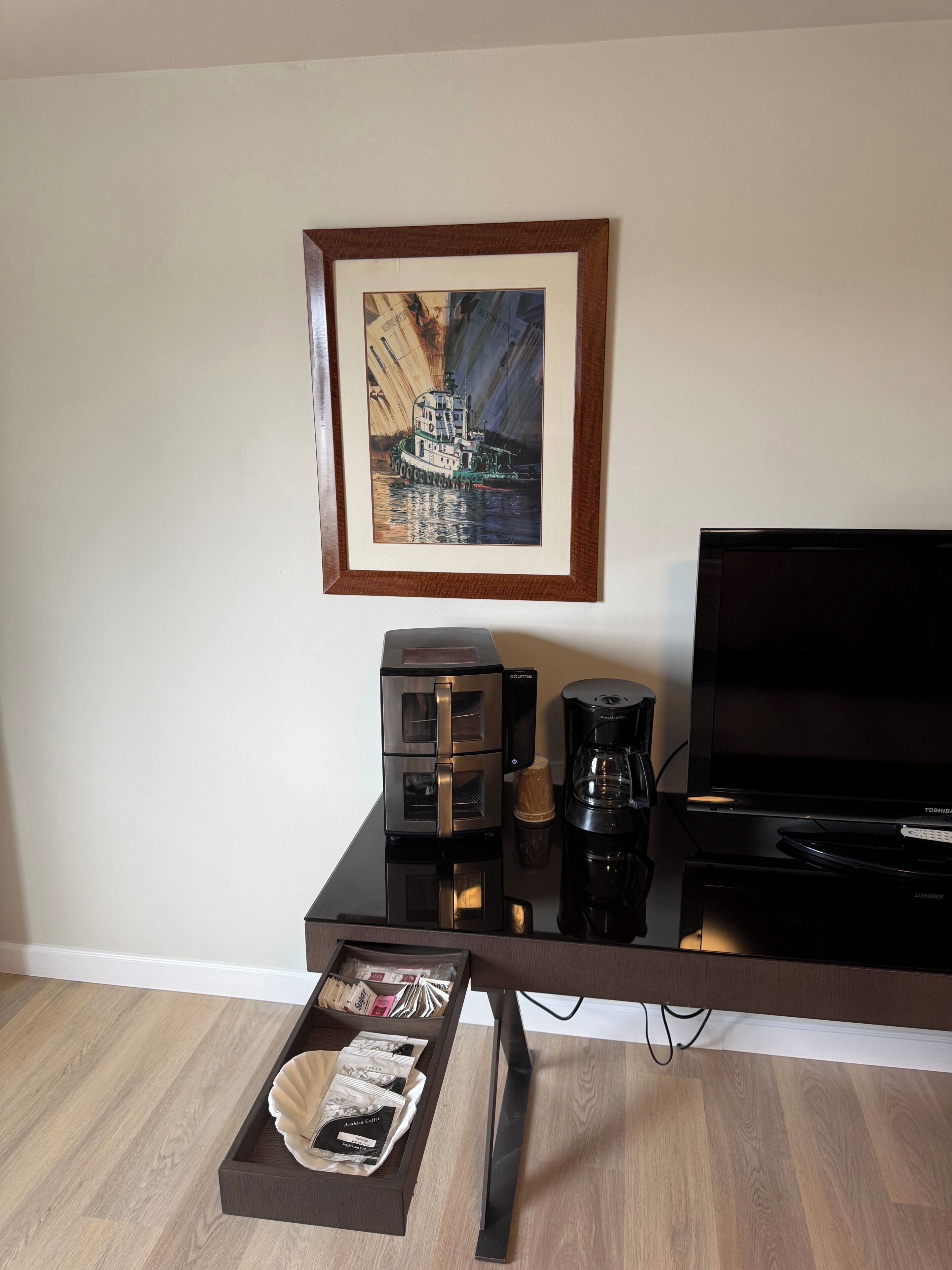 A modern living room with a flat-screen TV, a coffee maker, and a framed painting on the wall.