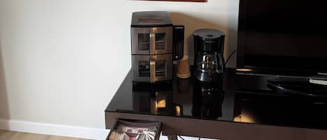 Una sala de estar moderna con un televisor de pantalla plana, una cafetera y un cuadro enmarcado en la pared.