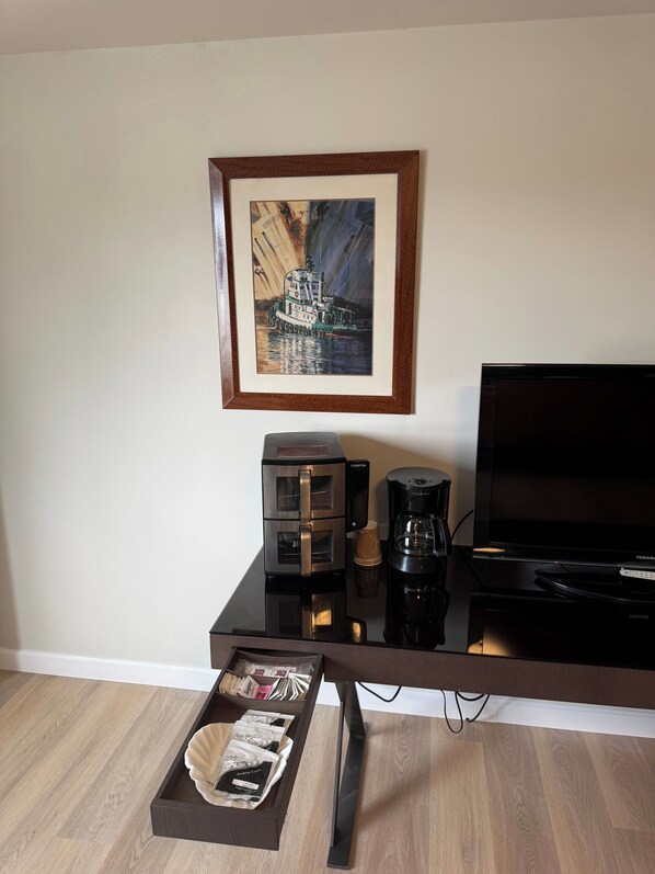 A modern living room with a flat-screen TV, a coffee maker, and a framed painting on the wall. - Naval Suites By FairBridge (Bremerton)