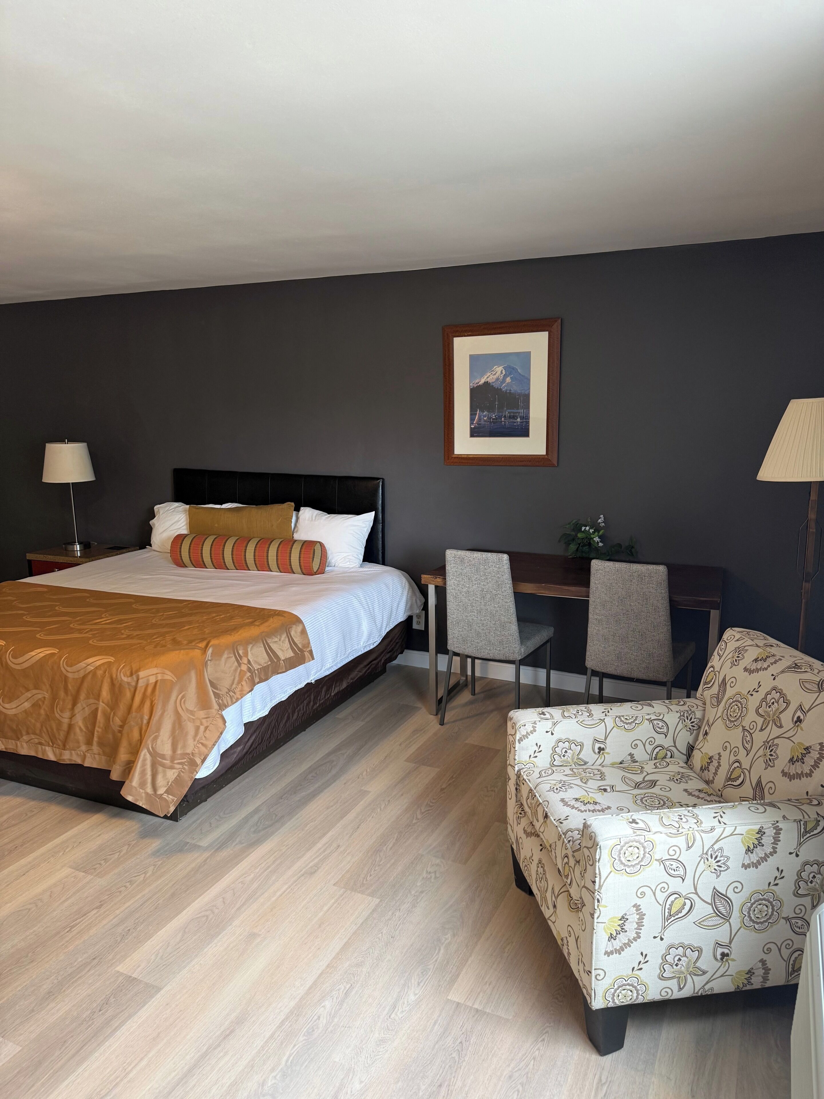 Una habitació d'hotel amb un llit, una taula de treball, una cadira i un quadre a la paret.