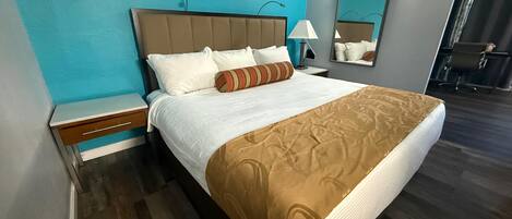 Una habitación de hotel con cama, mesita de noche, lámpara, espejo y una silla.