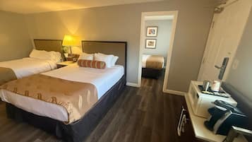 A hotel room with two beds, a bedside table with a lamp, a microwave, and a small kitchenette.