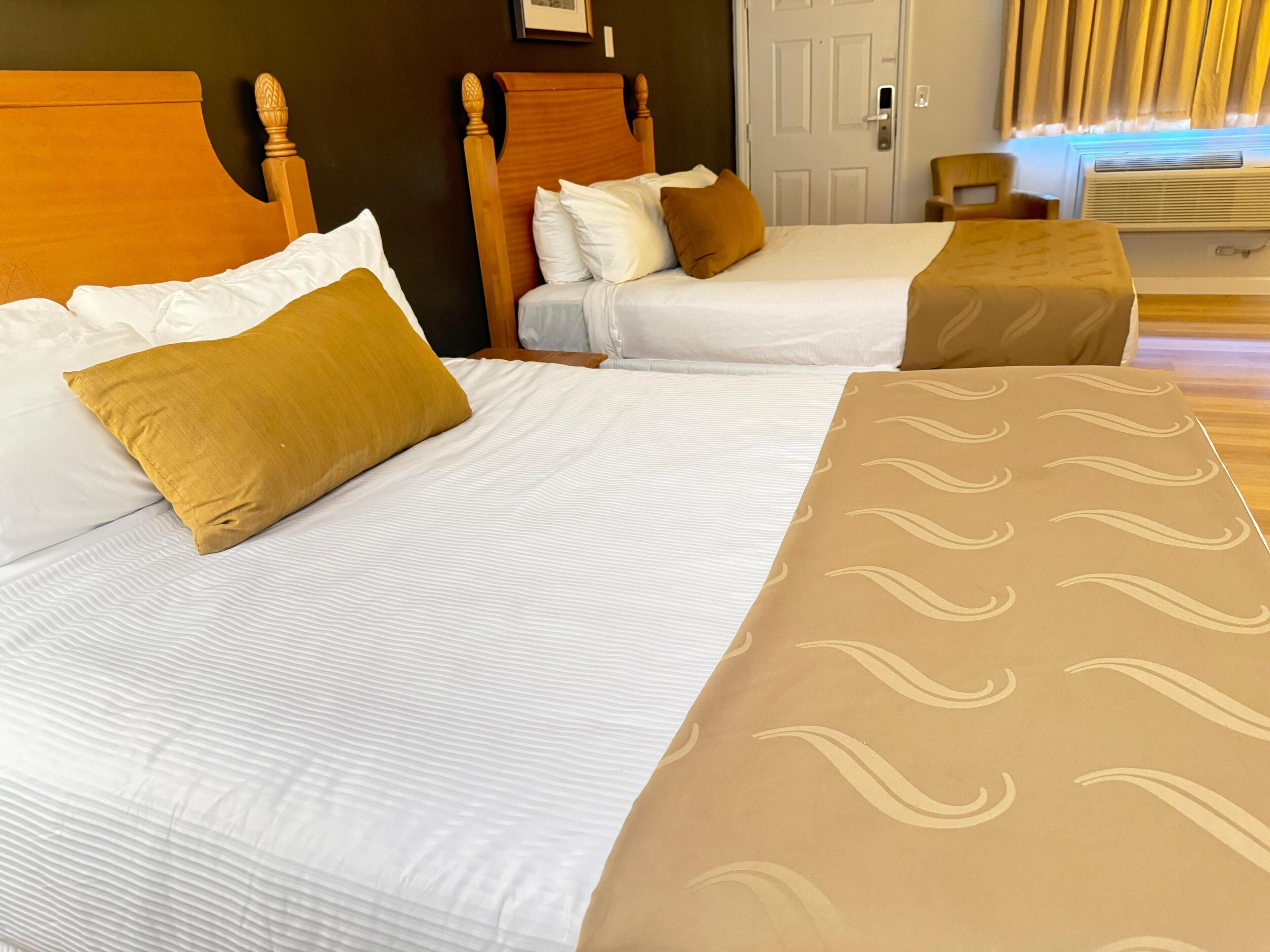 Two beds with wooden headboards, white bedding, and a brown patterned bedspread.
