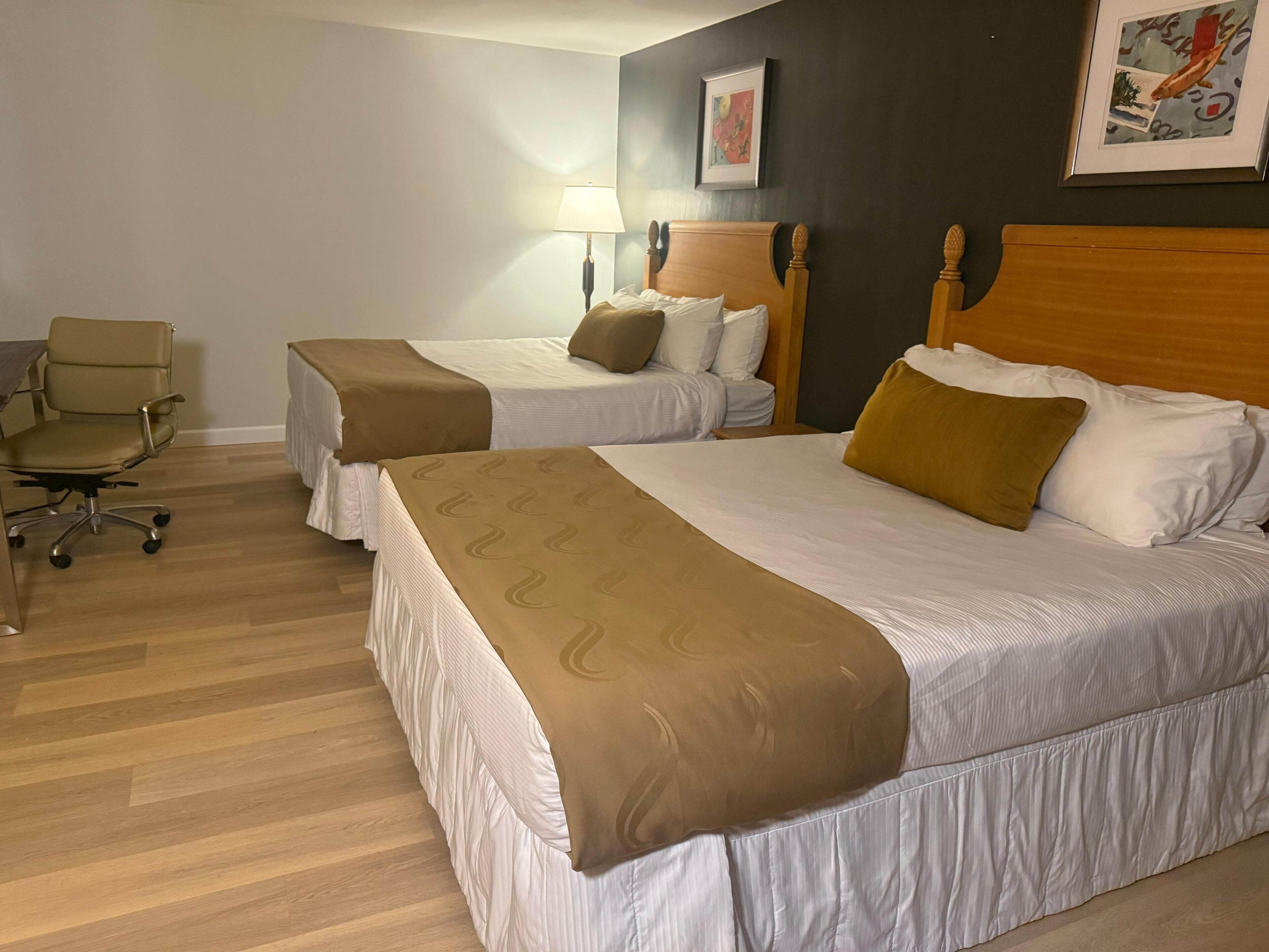 A hotel room with two beds, a desk, and a chair.