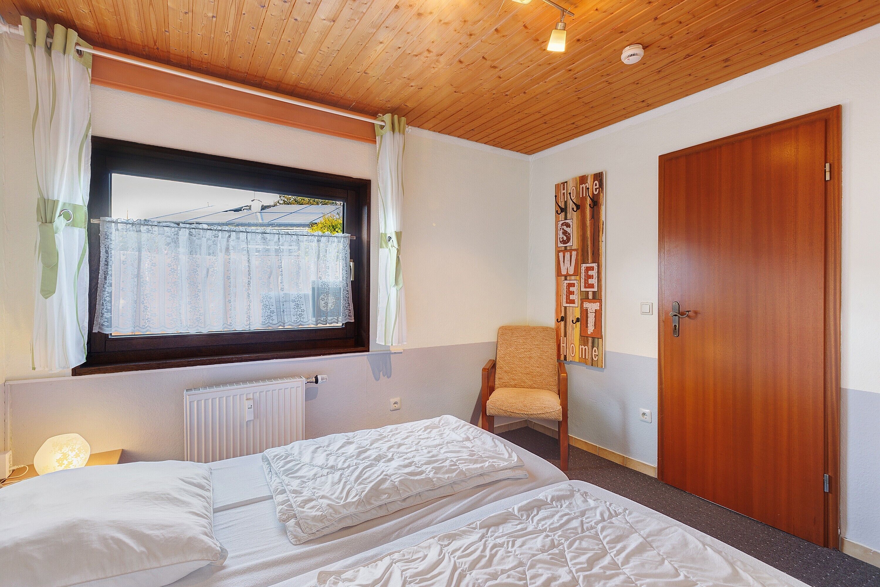 A bedroom with a bed, a chair, a wooden door, and a window with curtains.
