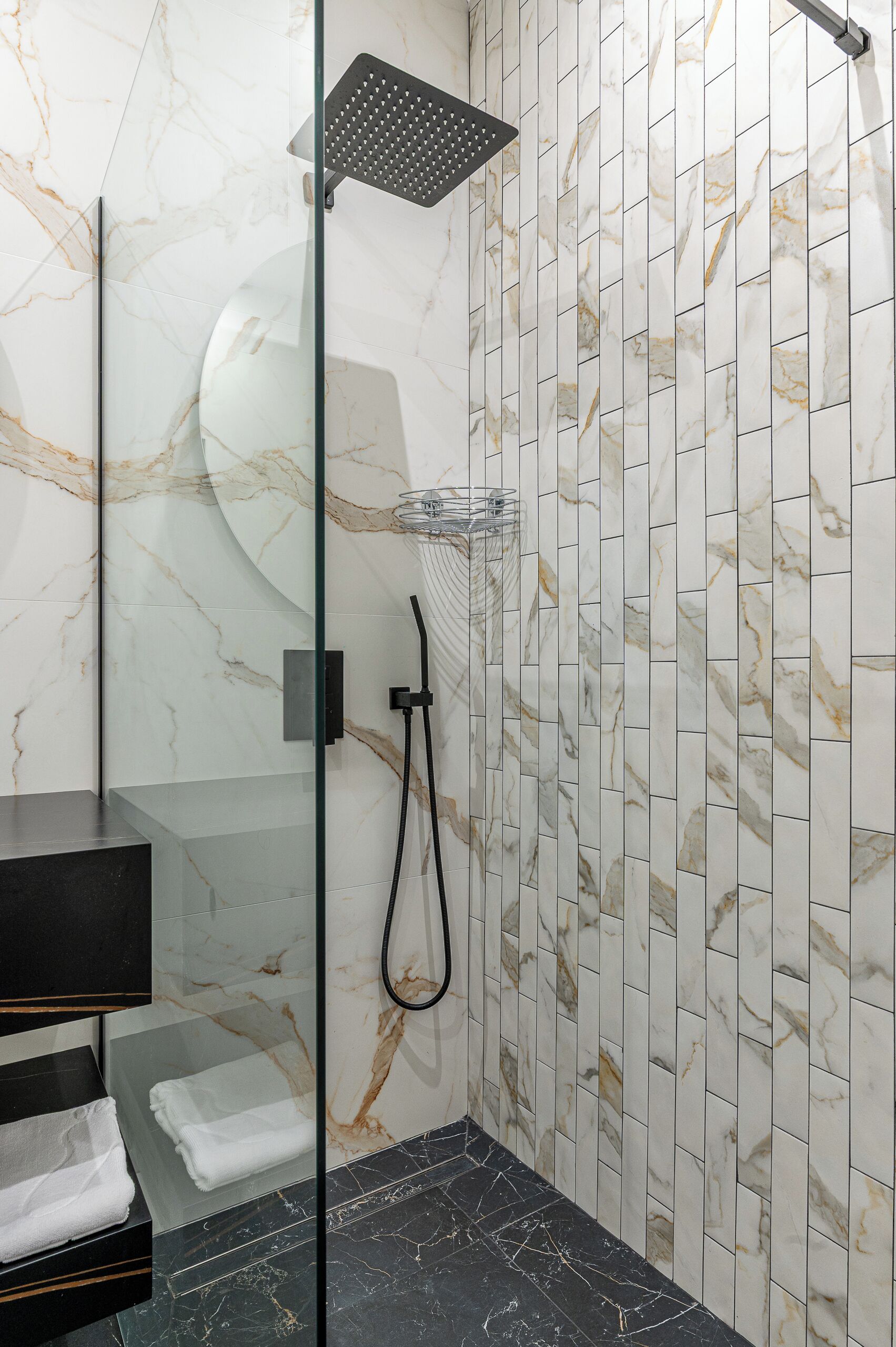 A modern bathroom with a glass-enclosed shower, marble walls, and a black marble floor.