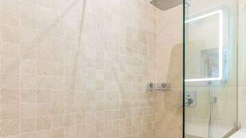 A glass-enclosed shower with a wooden floor, a tiled wall, and a white sink with a mirror.