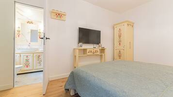 A bedroom with a bed, a television on a stand, a wardrobe, and a bathroom visible through an open door.