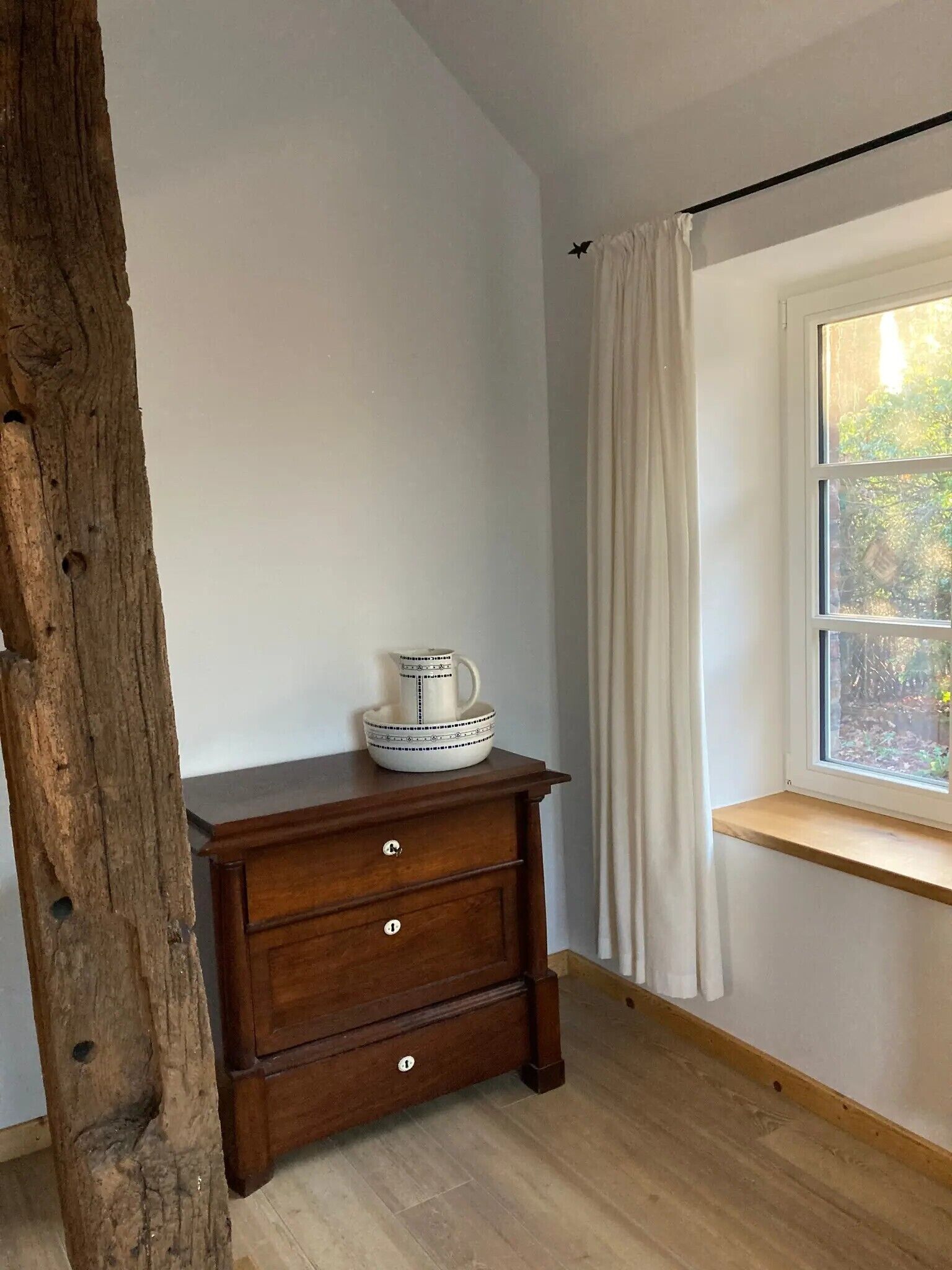 Una habitación con un aparador de madera, una ventana con cortinas y vistas al exterior.
