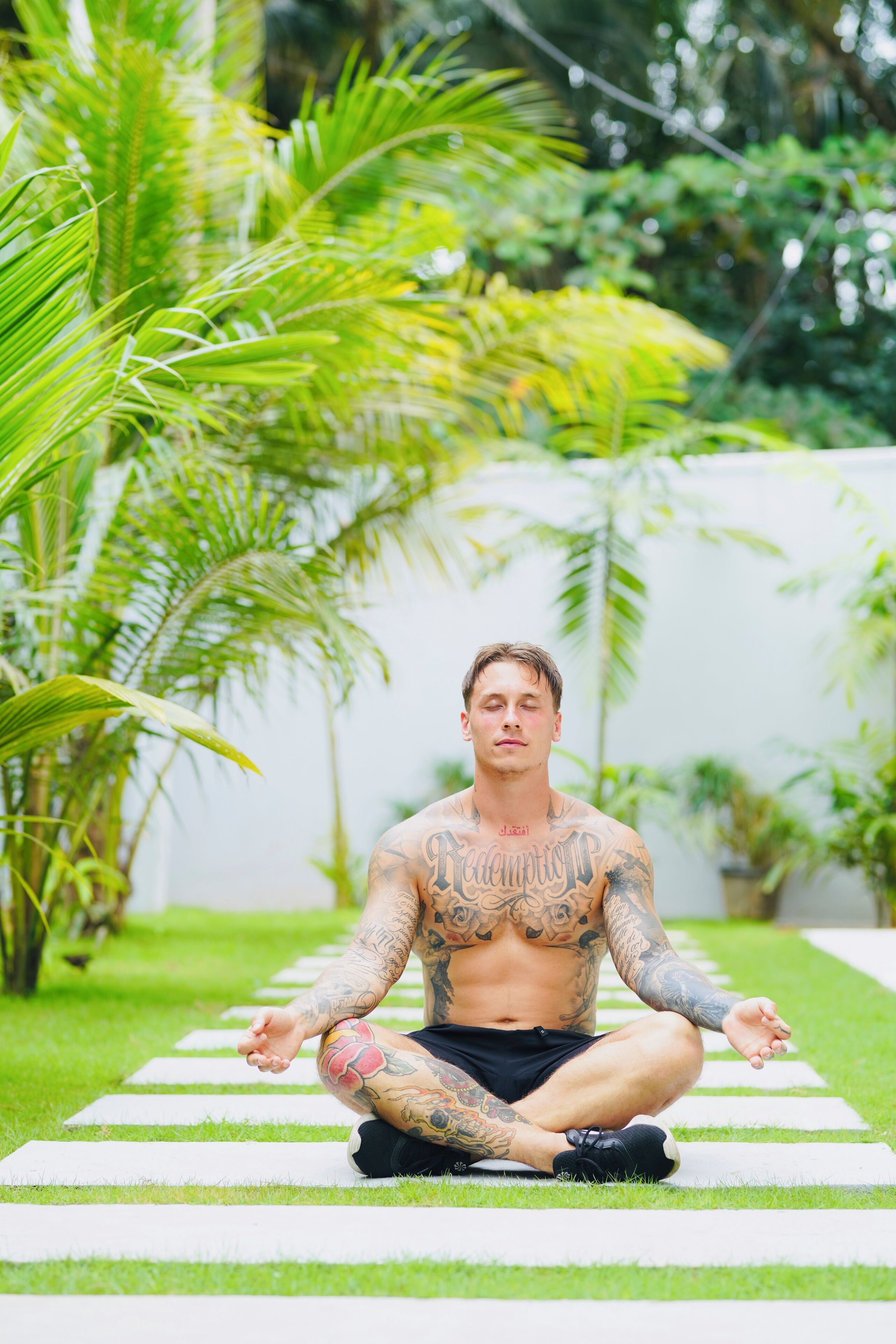 A person sitting cross-legged on a striped path in a garden with lush greenery.