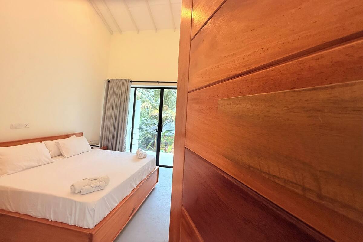 Une chambre avec un lit en bois, une fenêtre avec des rideaux et une vue sur la verdure.
