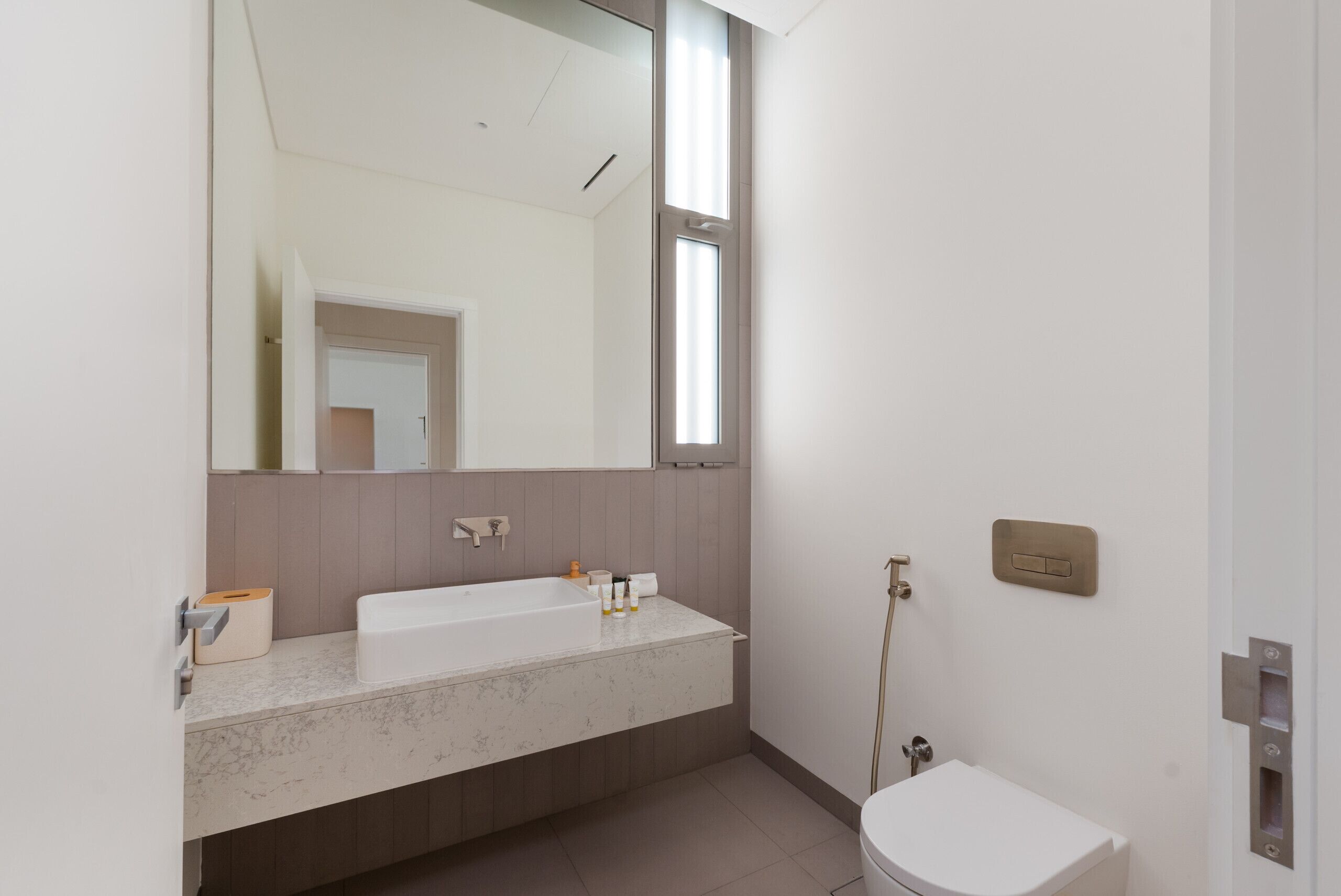 A modern bathroom with a large mirror, a white sink, and a toilet.