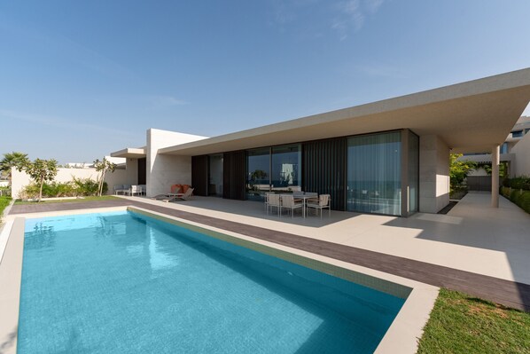 Una casa moderna con piscina, mobiliario exterior y grandes ventanales.