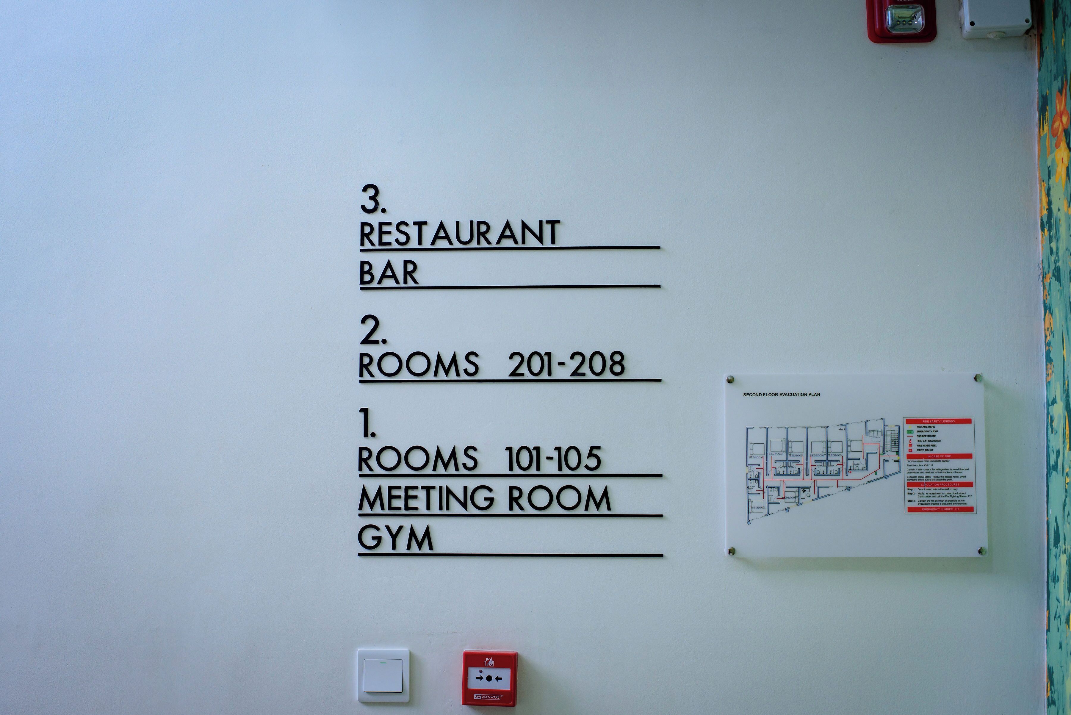 Una pared con una lista numerada de habitaciones y servicios, incluyendo restaurante, bar, habitaciones 201 a 208, sala de reuniones y gimnasio.