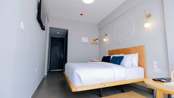 A modern hotel room with a wooden bed, a bedside table, a TV mounted on the wall, and a round wall decoration.