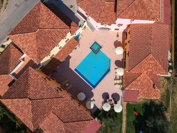 An aerial view of a hotel with a central swimming pool surrounded by outdoor seating areas and a covered patio. - Apartment With Shared Pool (Orosei)