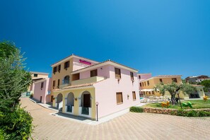 A multi-story hotel with a pink facade, balconies, and a pool area. - Apartment With Shared Pool (Orosei)