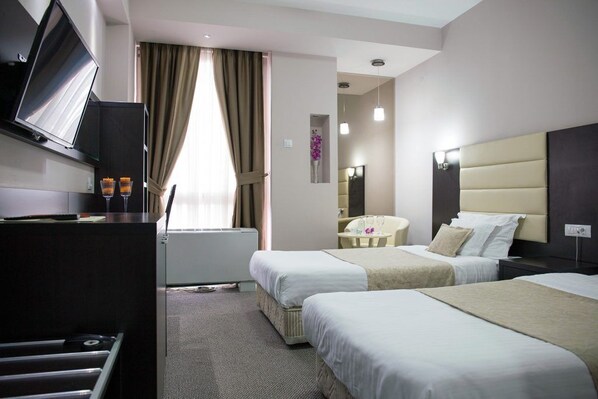 A hotel room with two beds, a desk with a TV, a small table, and a mirror. - Hotel Continental (Skopje)
