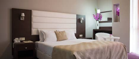 Una habitación de hotel con una cama grande, una mesita de noche, un tocador, un espejo y una pequeña mesa con un florero.