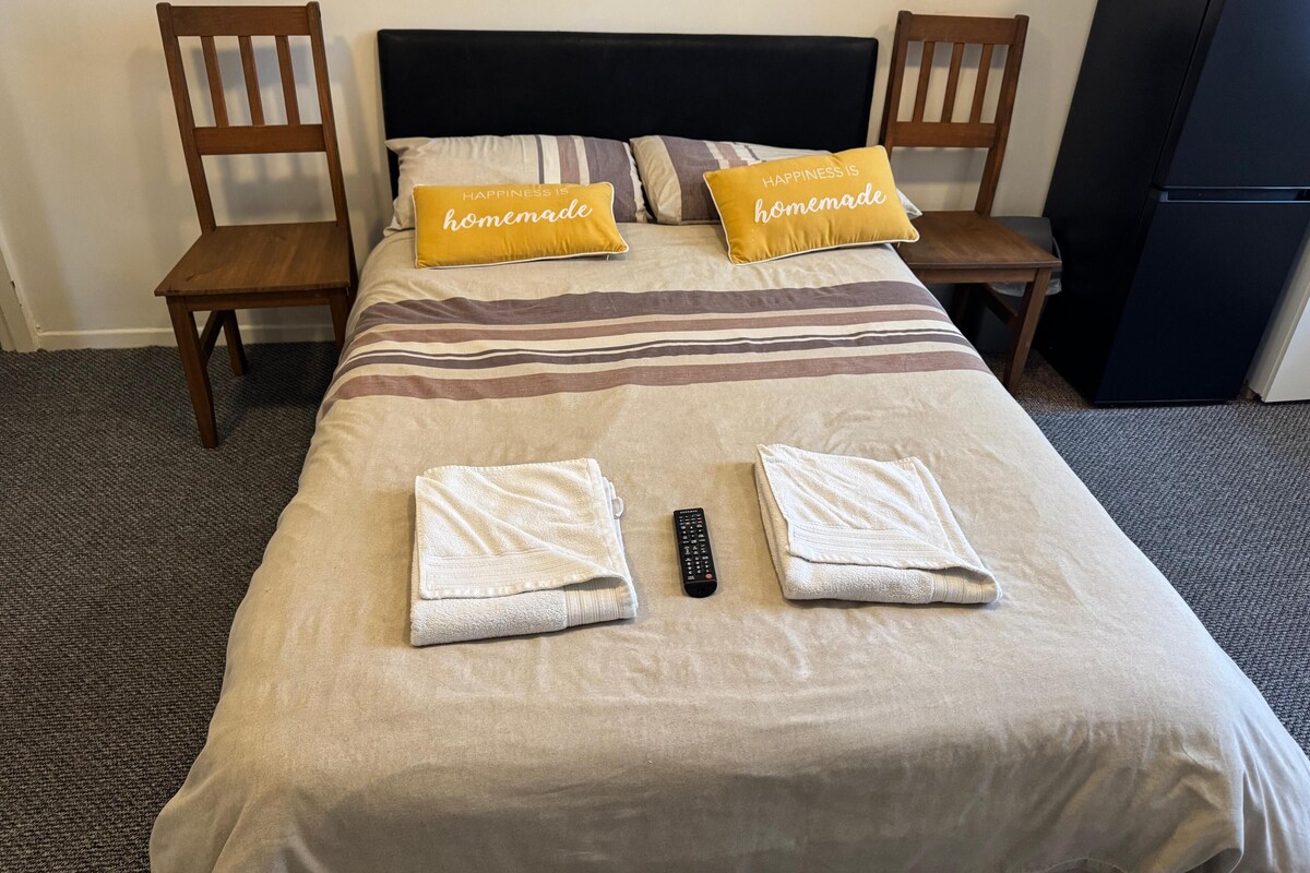 A neatly made bed with two pillows, two folded towels, and a remote control on a striped bedspread.